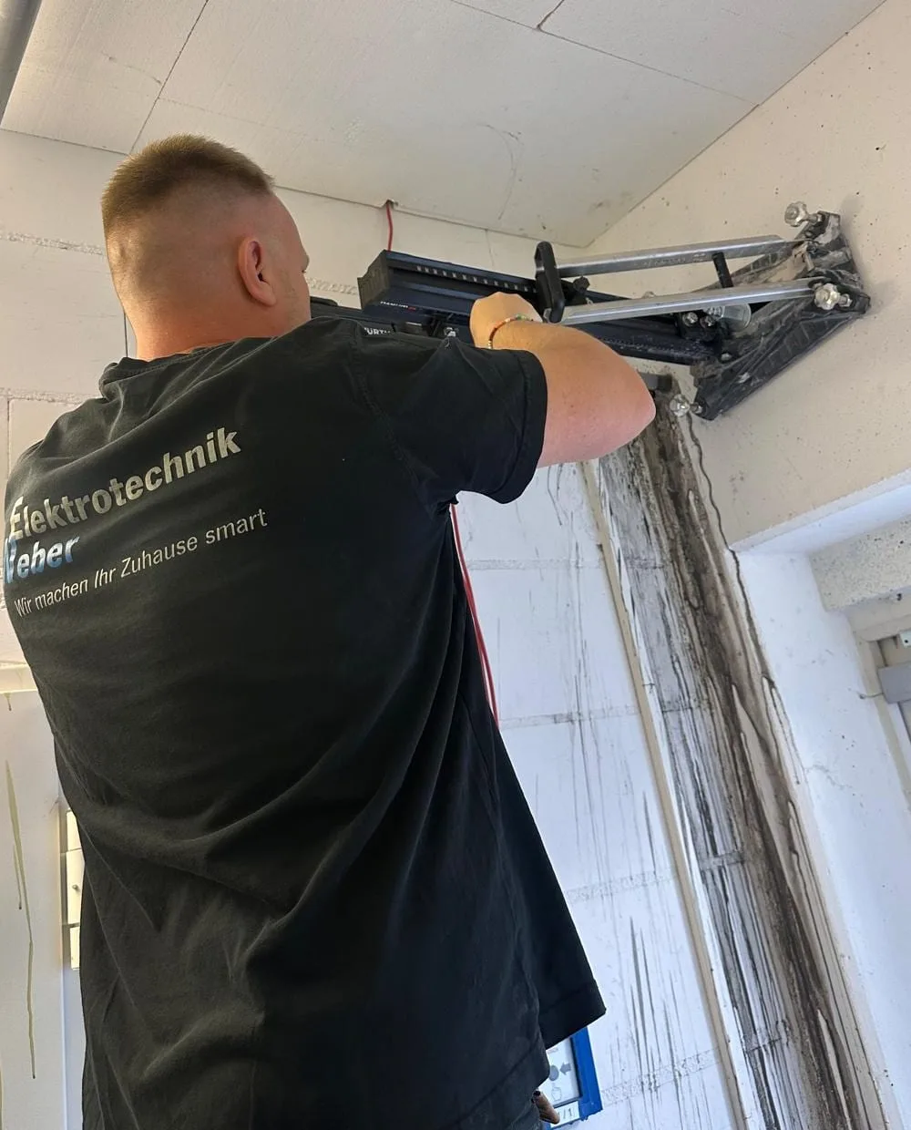 Monteur von Elektrotechnik Weber bei der Elektroinstallation, Firmenshirt mit Slogan Wir machen Ihr Zuhause smart